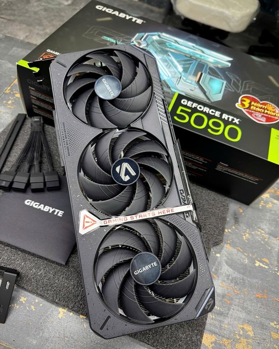 A Gigabyte GeForce RTX 5090 graphics card with three fans, displayed on top of its retail packaging on a workbench.