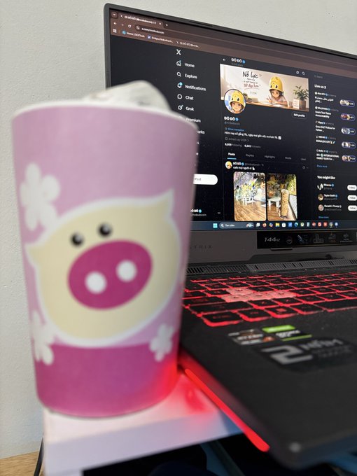 A pink mug with a cute pig face design sits next to a laptop displaying the X (formerly Twitter) interface, illuminated by red keyboard backlighting. The image complements the caption's message about quietly building on the social media platform, symbolizing the cozy, low-key dedication to growing on X day by day.