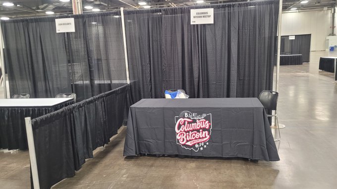 A black-draped table with a "Columbus BISCUITS" logo sits in a large convention hall near empty booths labeled "COLUMBUS BUTTERMILK MAFTUL" and "THIS WEEKEND".
