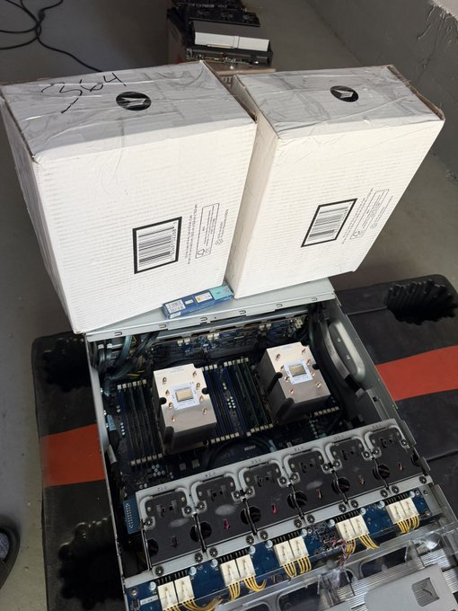 Two large white shipping boxes labeled "HSCBL" sit atop an open server chassis containing a dual-socket motherboard with two large heatsinks and multiple hot-swap power supply bays, suggesting the poster received used server GPUs in a repurposed enterprise system.