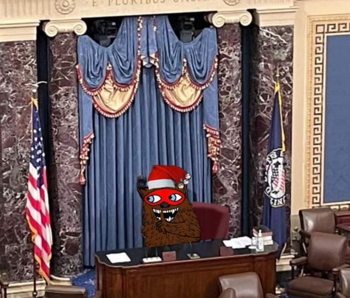 A cartoon Sasquatch wearing a red MAGA hat and red mask sits behind the presiding officer's desk in the U.S. Senate chamber, flanked by the American flag and Senate flag, with "E PLURIBUS UNUM" visible above the blue drapery. The image humorously personifies Senate leadership amid discussion of Majority Leader John Thune canceling the August recess, suggesting he will be watching over the proceedings.