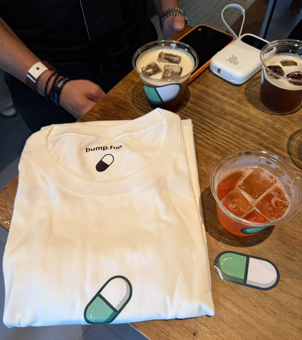 A folded white t-shirt printed with "pump.fun" and a green-and-white pill logo sits on a wooden bar counter alongside three cocktails in branded cups, with a person's arm wearing a wristband visible in the background. The branding ties directly to the post's bullish sentiment about Pump.fun, suggesting a branded promotional or community event.