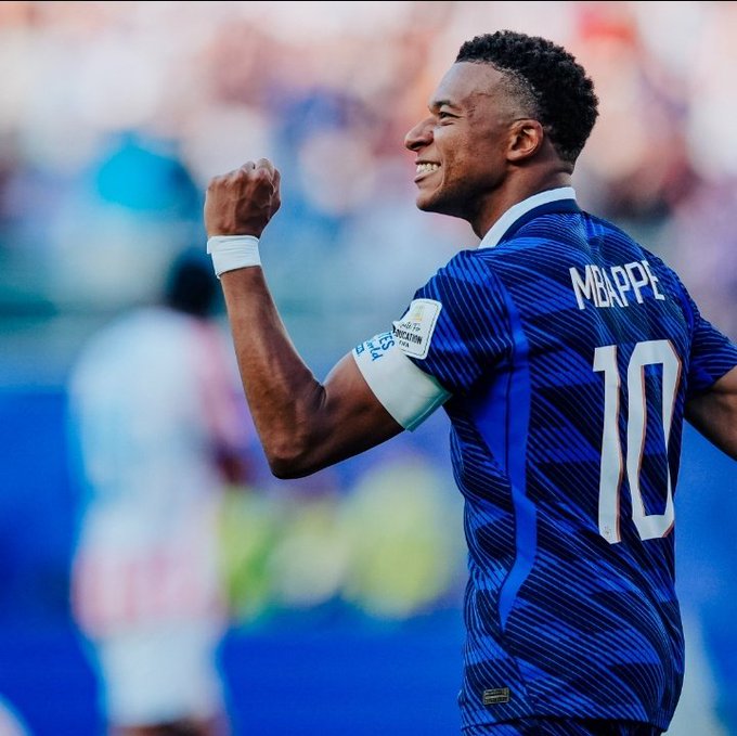 Kylian Mbappé, wearing jersey number 10 for France, celebrates a goal during the knockout stage of the World Cup with a triumphant fist pump and a smile, aligning with the post's celebration of his goal-scoring achievement.