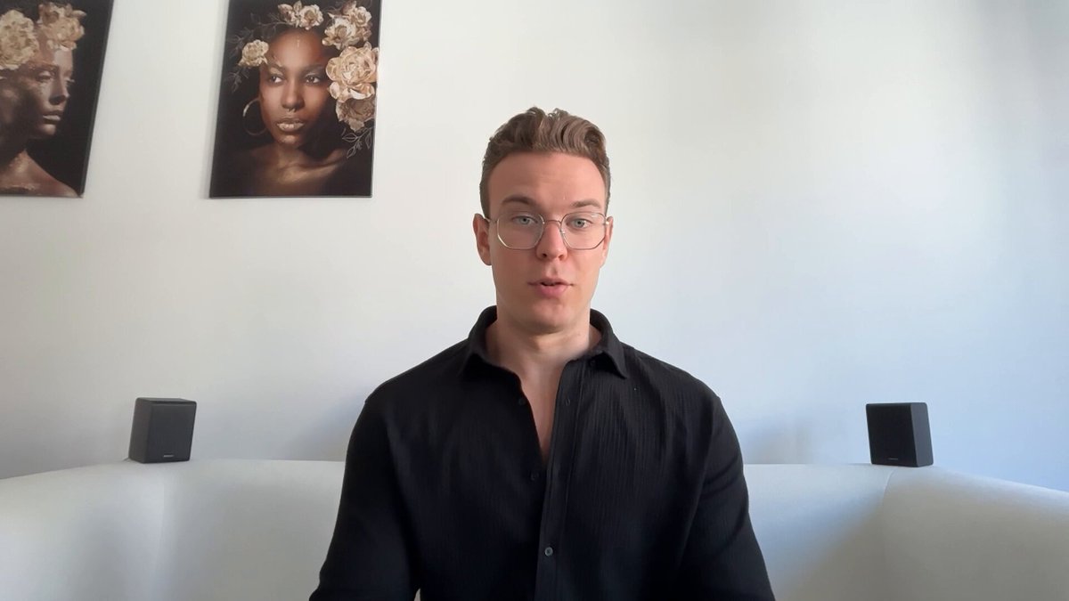 A man with glasses and a black shirt speaks directly to the camera in a room with portrait artwork and speakers, promoting an inclusive hiring opportunity and inviting viewers to join his Discord community for more details.