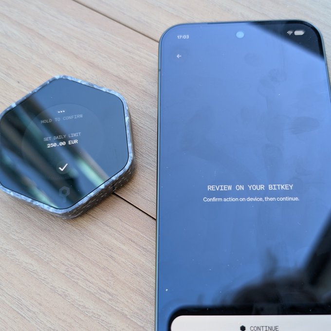 A Bitkey hardware wallet and smartphone display a setup screen where the user can set a daily spending limit of 250.00 EUR with the option to "HOLD TO CONFIRM," illustrating how the wallet enables on-device spending controls without requiring the full Bitkey for small transactions.