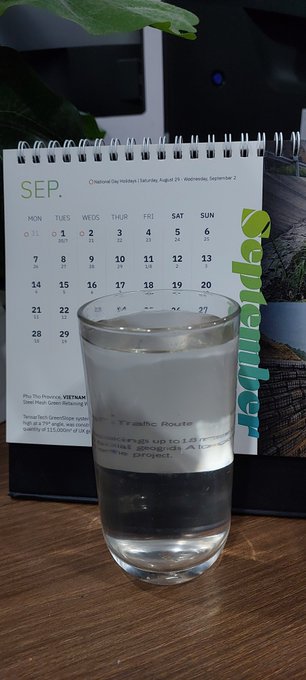 A glass of water sits on a wooden table in front of a small September calendar with a green plant visible in the background.