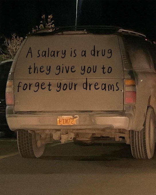 The dusty rear window of an SUV bears the handwritten message "A salary is a drug they give you to forget your dreams."