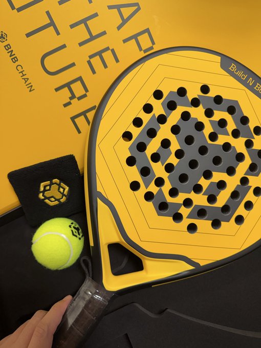 A yellow padel racket with 'ATHLET' and 'BNB CHAIN' branding alongside a tennis ball and wristband.