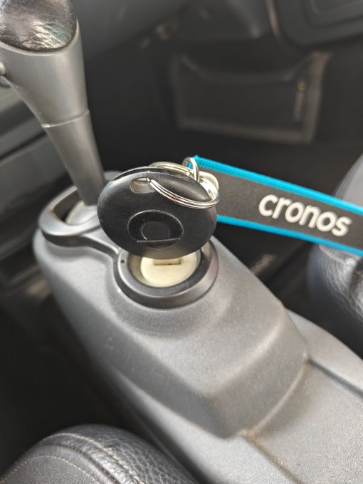 A car key rests in the ignition with a "cronos" branded lanyard attached, humorously hinting at the Cronos ($CRO) burn mentioned in the post. The image plays on the word "crypto" sounding like the car's ignition starting, suggesting the burning or destruction of $CRO tokens.