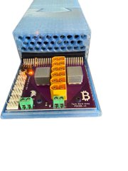 An electronic component mounted on a blue printed circuit board featuring orange capacitor arrays, green terminal blocks, and other electronic components.