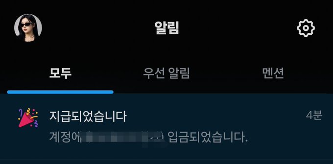A smartphone screenshot in Korean showing an "알림" (Alerts) page with a 4분 (4 minutes) old notification that says "지금되였습니다" (Just now). The notification text reads "계정에 [blurred username] 입금되였습니다" meaning "[blurred name] has been deposited into the account," which appears to confirm a successful payment transaction related to the celebratory post about completing a historic weekly X payment.