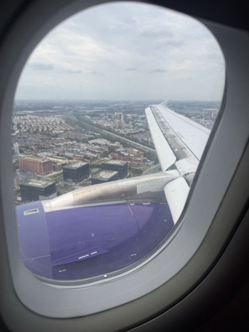 A view from an airplane window shows the wing of the aircraft descending toward Shanghai, with the city's urban sprawl visible below under an overcast sky. The image complements the caption by capturing the moment of arrival in Shanghai, where the traveler had rushed to attend a Solana event after unexpectedly receiving an important message.