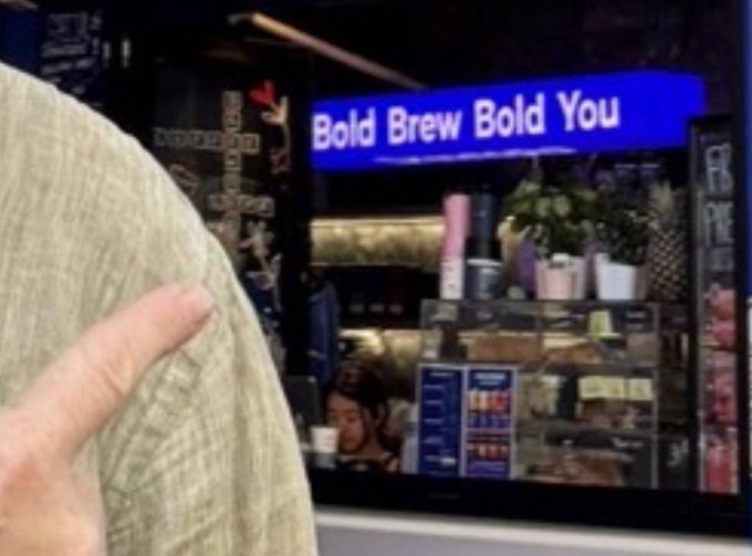 A photograph of a storefront sign reading 'Bold Brew Bold You' with a person's hand and torso visible in the foreground.