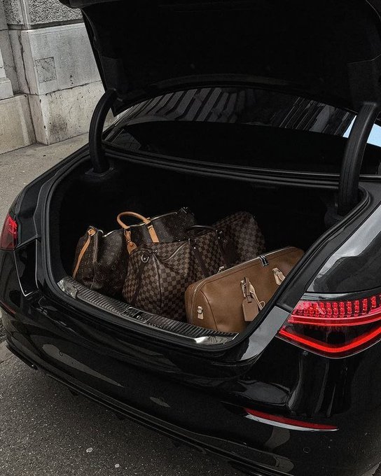 The open trunk of a black car packed with several Louis Vuitton designer bags and luggage.
