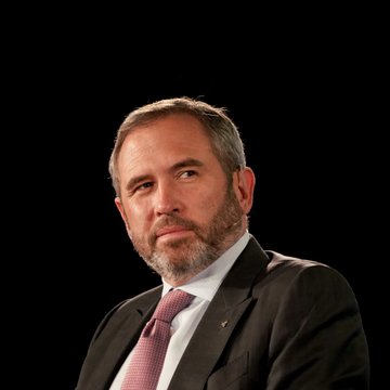 A man with a beard, wearing a dark suit, white shirt, and pink tie, appears against a black background, identified by the accompanying post as Ripple CEO Brad Garlinghouse. The image accompanies his statement advocating for the U.S. to become the crypto capital of the world ahead of the Senate's upcoming CLARITY Act cloture vote.