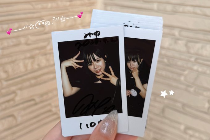 A hand holding two signed polaroid photos of a young woman with the name 'City' visible, decorated with drawn hearts and sparkles with text 'シイ☆' and '★★'.