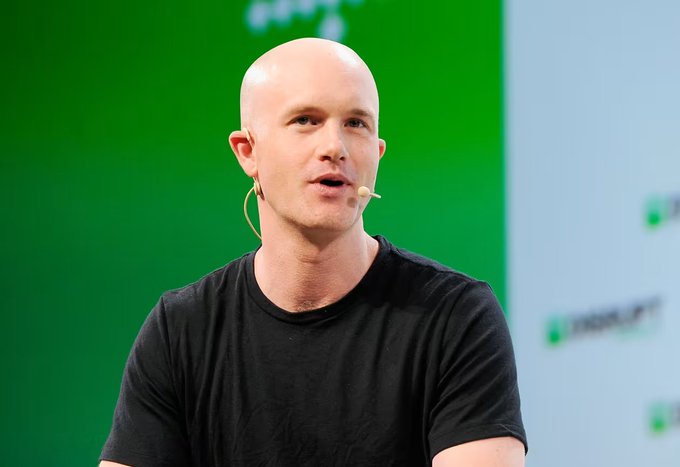 A bald man wearing a black t-shirt and a headset microphone, appearing to speak at a conference or tech event with a green and white background.