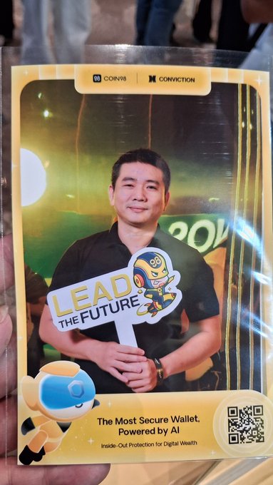 A man in a black shirt holds a "LEAD THE FUTURE" sign with a mascot at a COIN98 and CONVICTION event, displayed on a promotional card reading "The Most Secure Wallet, Powered by AI - Inside-Out Protection for Digital Wealth" with a QR code.