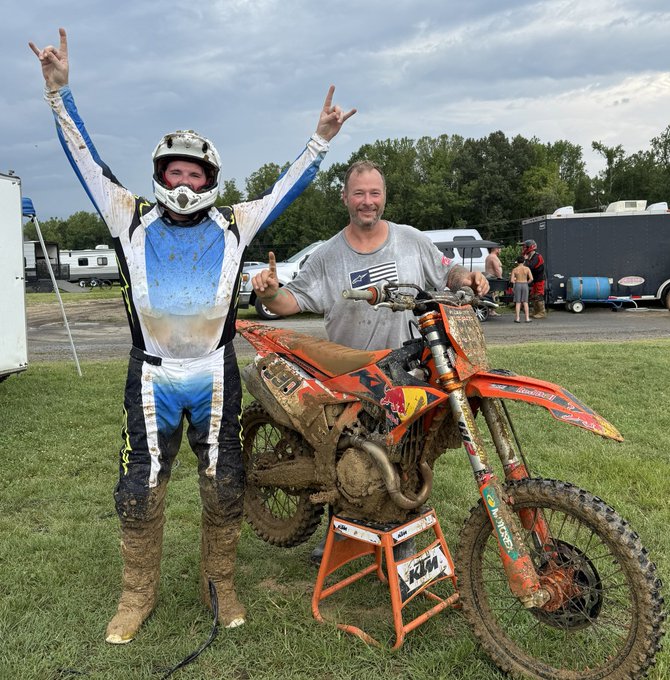 A muddy motocross rider in blue and white gear raises both arms in victory next to a smiling man holding a KTM 450 dirt bike covered in mud, sponsored by Market Cipher and Polymarket.com, after winning 1st overall in the 30+A/B class and 2nd in the 35+ class.