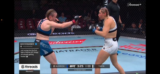 Two female UFC fighters, identified as Aldrich and Tarin, face off in the octagon during a flyweight bout at 3:25 in round 1, while a social media post from @mayceebarber is overlaid on the screen.