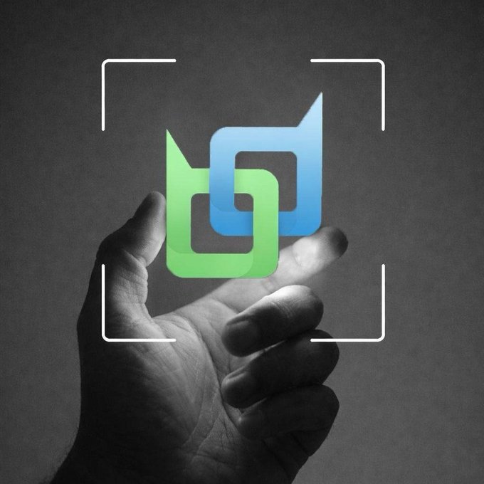 A grayscale photograph of a hand holding a glowing, stylized blue and green logo within a white viewfinder frame against a dark background.