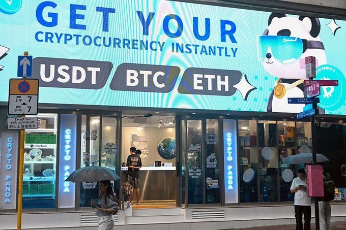A storefront with a large illuminated sign reading 'GET YOUR CRYPTOCURRENCY INSTANTLY' featuring USDT, BTC, and ETH options alongside a panda mascot wearing VR goggles, with 'CRYPTO PANDA' written on the windows.