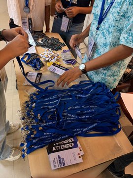 A table covered with blue lanyards and attendee badges at what appears to be a conference or event registration area, with a person wearing a lanyard visible.