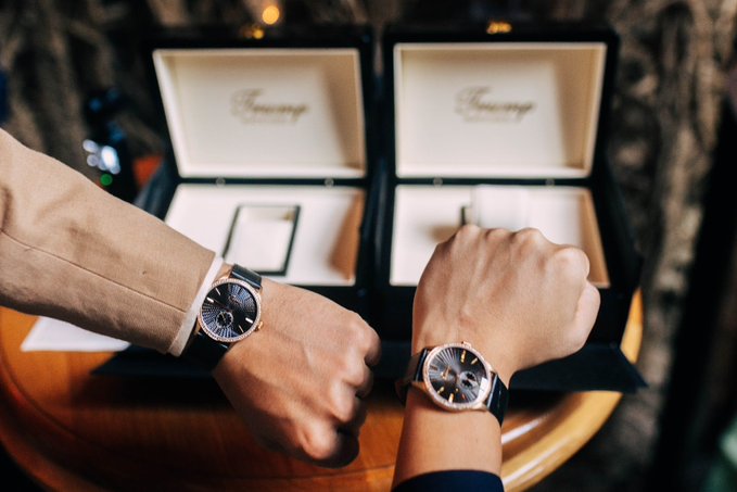 Two people bump their fists together to compare their wristwatches, with two open Chopard watch boxes displayed on a table in the background.