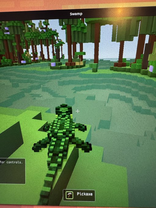 A Minecraft-style video game screenshot shows a pixelated crocodile/alligator in a swamp environment, with a pickaxe tool selected at the bottom of the screen.