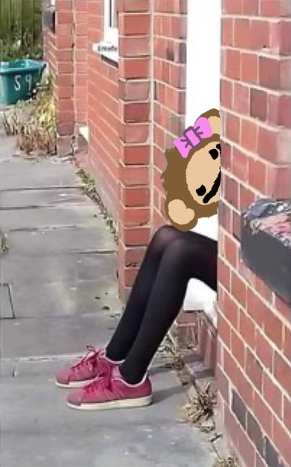 The image features a person sitting on a brick wall, with their legs crossed over each other. They are wearing black tights and red shoes. The person's head is resting against the brick wall, giving an impression of them being "stuck" or "caged". In the background, there is a house visible behind the person.