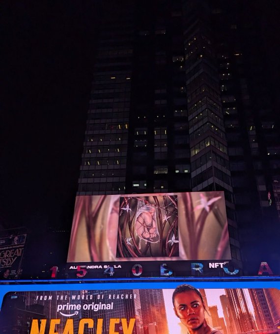 A nighttime photo of a Times Square billboard displaying a floral artwork above an advertisement for the Amazon Prime original 'Reacher', with a tall dark skyscraper in the background.