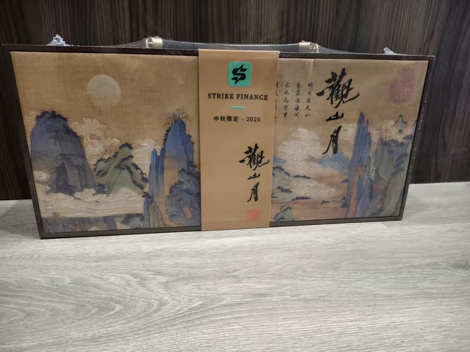 A gift box with a brown ribbon labeled 'STRIKE FINANCE' and '中秋限定 · 2026', featuring traditional Chinese landscape artwork and the characters '觀山月'.