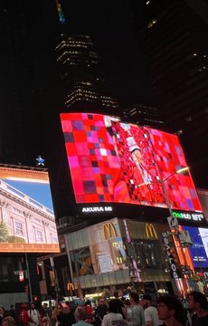 Nighttime photo of a large illuminated billboard in Times Square or a similar urban setting, displaying a pink and red pixelated image with the brand 'AQUA' visible below, surrounded by city buildings including a McDonald's.
