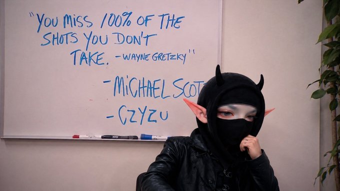 A person dressed in a black ninja/elf costume posing in front of a whiteboard that reads "YOU MISS 100% OF THE SHOTS YOU DON'T TAKE. - WAYNE GRETZKY" with additional signatures "- MICHAEL SCOTT" and "- GZYZU."
