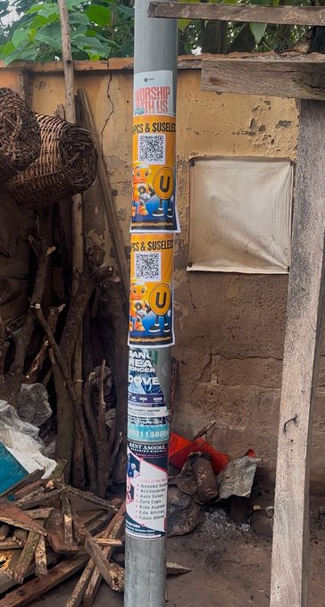 A utility pole is plastered with promotional flyers advertising "AIRSHIP NFT USELESS" and "$USELESS" tokens, complete with QR codes and cartoon graphics, while firewood and rustic items lean against the mud-brick wall behind it. The image visually demonstrates the creator's dedication, showing they printed physical flyers and took the "unipcs and $USELESS" project offline into the real world rather than just relying on online memes.
