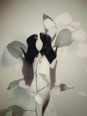An abstract double-exposure style portrait blending black high-heeled shoes with delicate white flower petals against a soft beige background.