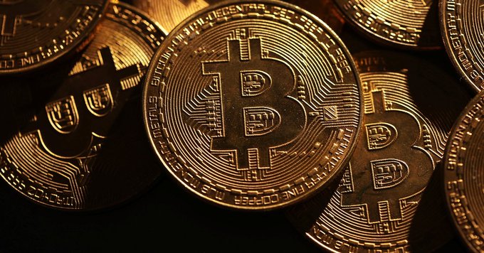 A close-up photograph of several physical Bitcoin tokens with the distinctive 'B' logo, illuminated in warm, golden light.