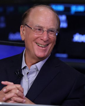Larry Fink, CEO of BlackRock, smiles warmly during an interview, his expression reflecting the positive momentum referenced in the post about surging institutional demand for Bitcoin and Ethereum ETFs, including BlackRock's offerings.