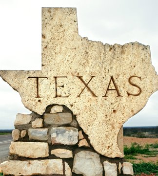 The image features a large stone sign that reads "TX" with the word "Texas" written in black letters, positioned above a rock wall. The sign appears to be made of stone or concrete blocks, giving it an old-fashioned appearance. The text on the sign is in black, which contrasts with the white background and makes it stand out prominently. The image also includes some text that reads "TEXAS OFFICIALLY APPOINTS MEMBERS TO THE TEXAS strategic bitcoind advisory committee they're ACTIVELY BUILDING THE operational rails for a Bitcoin reserve". This message suggests that the sign is related to Bitcoin or cryptocurrency, possibly indicating an event or gathering related to this digital currency.