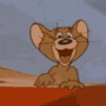 The image features a cartoon mouse with big ears, sitting on top of an orange surface or red object. The mouse appears to be smiling and has its mouth open wide, giving off a happy vibe. The background is a light blue color that contrasts nicely with the orange surface where the mouse is sitting. There are no other objects in the image besides the cartoon mouse and the orange surface it's on.