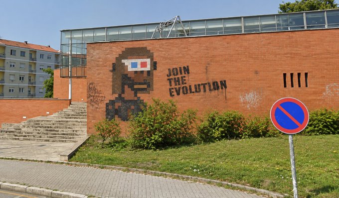 A brick wall with a pixelated mural of a face wearing 3D glasses and the text 'JOIN THE EVOLUTION' alongside four tally marks, with a no-parking sign in the foreground.