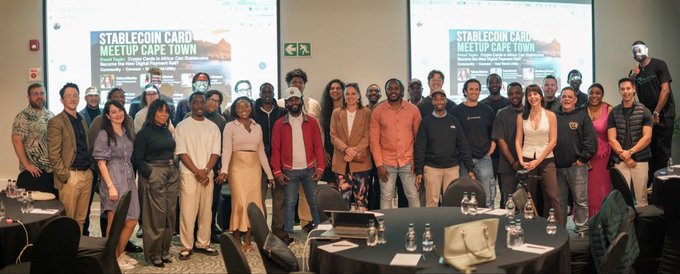 A group photo of attendees at the 'Stablecoin Card Meetup Cape Town' event, with slides on screens behind them and a panel featuring 'Pi Network' branding and representatives from Capa.Up, Solana, Xeni Fintech, and Capacorn.