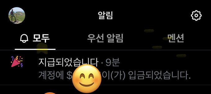 A Korean-language notification interface displays a message stating '지금되었습니다' (It's been done) and '계정에 $이(가) 입금되었습니다' (has been deposited to your account), accompanied by a smiling emoji.