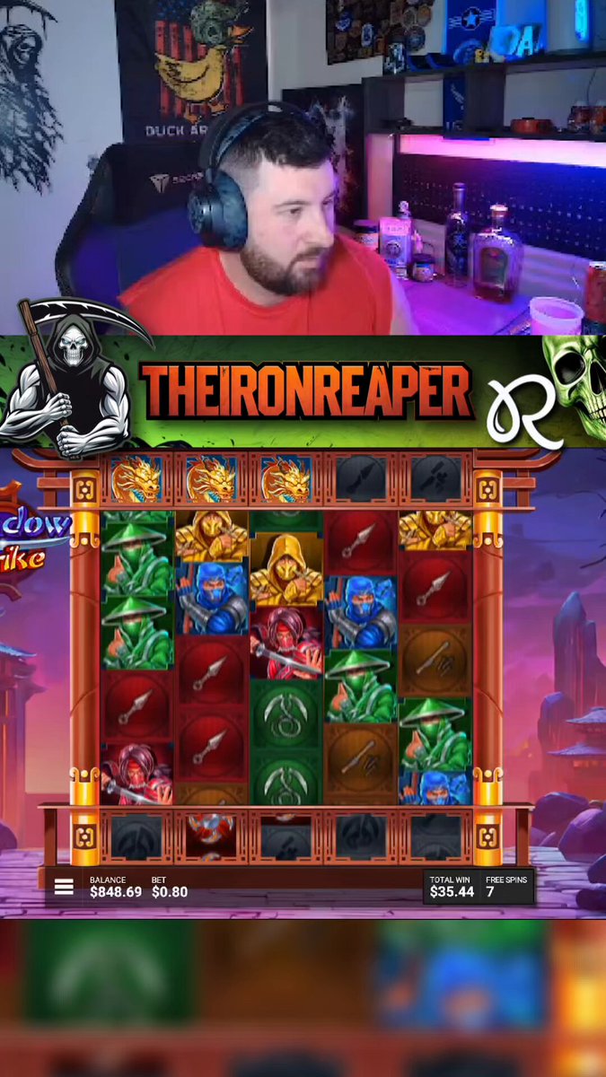 The image shows a man wearing headphones sitting at a slot machine, likely playing a game of slots or btc. The slot machine has a large screen displaying various symbols and numbers, indicating that the player's outcome could be uncertain. The surrounding area also features a poster with a skull on it, adding to the overall theme of gaming and entertainment.