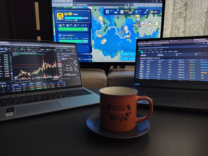 A multi-monitor trading and gaming setup featuring a laptop showing a candlestick chart, a center monitor displaying a Wowsdaypirates game map, and a right monitor with trading data, accompanied by an orange 'COFFEE' mug on a saucer in the foreground.