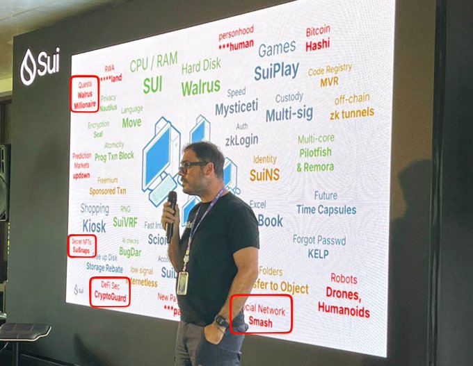 A man in a black t-shirt speaking into a microphone at a Sui presentation, standing before a large screen displaying a word cloud of Sui ecosystem terms including SuiPlay, SuiVRF, Walrus, and DeepBook.
