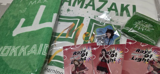 The image shows a collection of merchandise items, including a green towel with white text that reads "stepn", two small bags labeled "rayo light", and three stickers featuring a girl's face. The items are arranged next to each other on a surface, creating an organized display for sale or distribution.