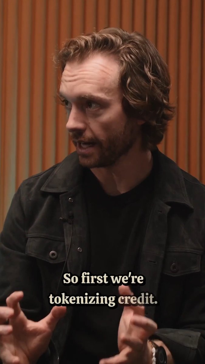 A man with curly hair and a beard, wearing a black jacket, speaks while gesturing with his hands. The caption reads, "So first we're tokenizing credit," and contextualizes the discussion around pactfinance's onchain credit solutions powered by USA₮.
