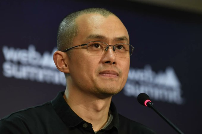 The image features a bald man wearing glasses, standing in front of a microphone with his hands at his sides. The background shows a banner that reads "WOW: A U.S. judge has dismissed a lawsuit that accused Binance and former CEO Changpeng Zhao (CZ) of enabling terrorism." This suggests that the image is related to a legal case or an event involving these two individuals, possibly in the context of cryptocurrency regulation or a public statement made by them.