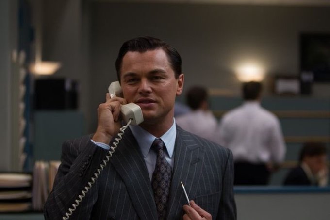 Leonardo DiCaprio as Jordan Belfort in The Wolf of Wall Street, wearing a pinstripe suit and talking on a white telephone in an office setting.